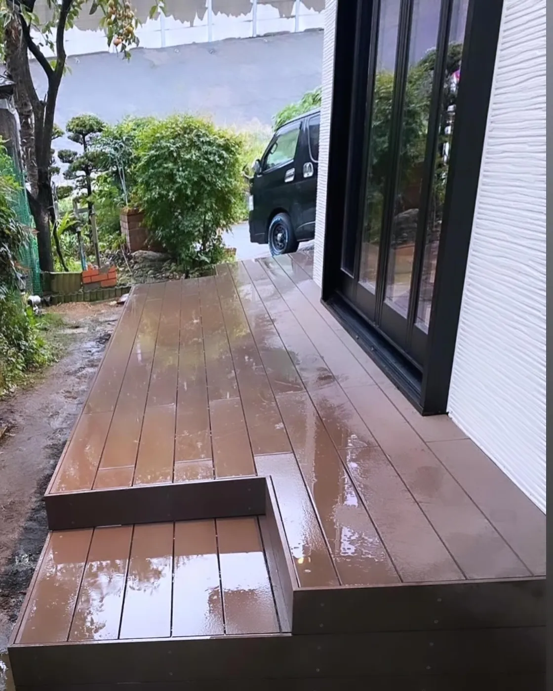 雨に濡れた濃褐色のデッキと、庭へ下りる踏み段